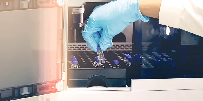 gloved hand handles a vial in a lab
